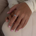 A hand with pink manicured nails wears the Open Toi et Moi Birthstone Ring, a silver ring adorned with two colorful gemstones.