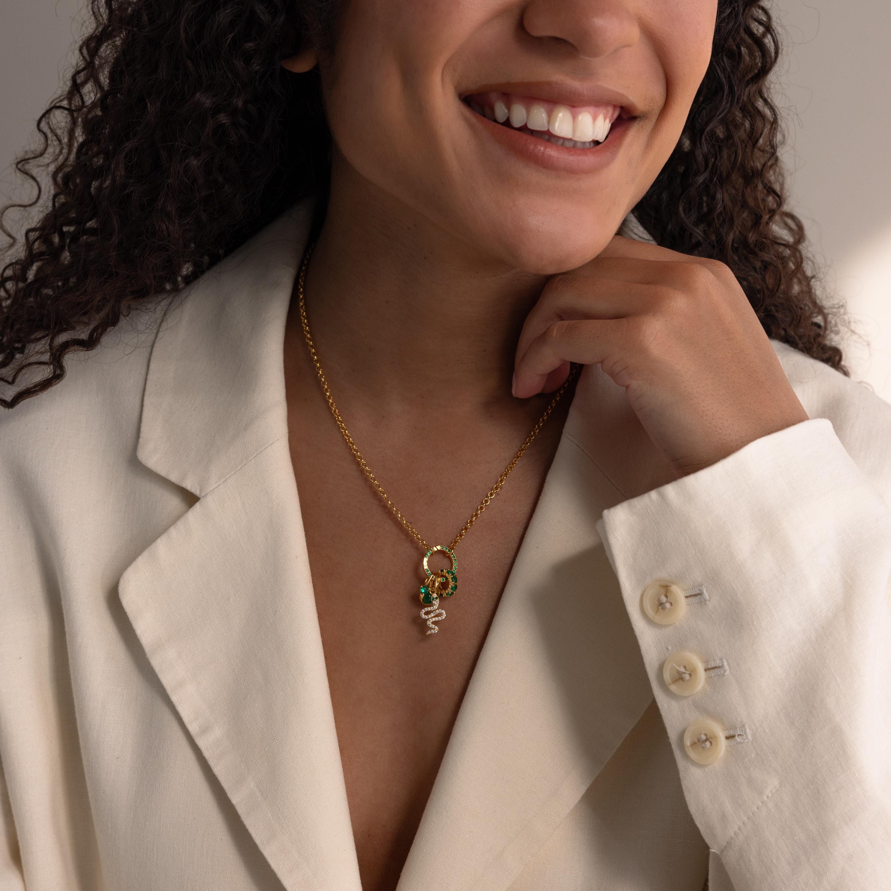 Woman in a cream blazer smiling, wearing personalized jewelry—a gold necklace featuring the Pave Blue Zircon Charm Clip pendant.