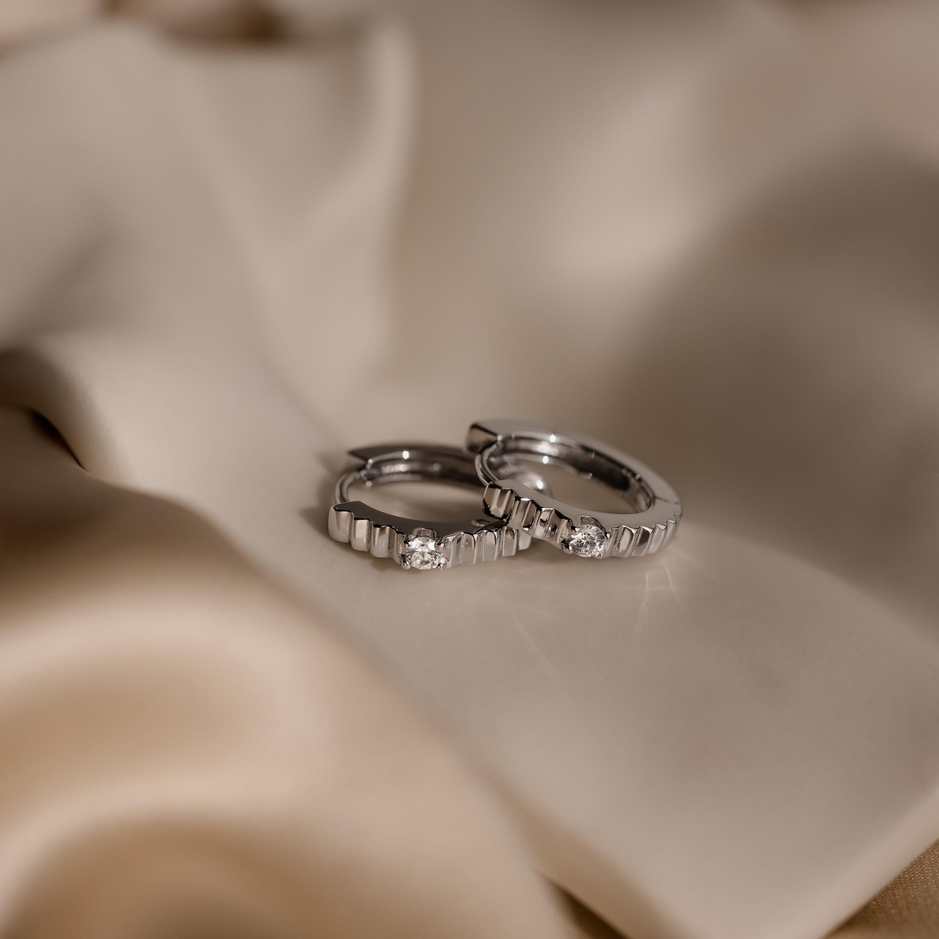 A pair of Diamond Ribbed Huggies sparkle with diamonds and a sleek ribbed design, displayed on smooth beige satin fabric.