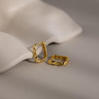 Two Hammered Rectangle Hoops with a wavy, geometric design are displayed on a neutral, curved surface.