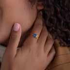 Close-up of a hand wearing the Toi et Moi Oval Birthstone Ring with blue and yellow stones, touching the side of the face.