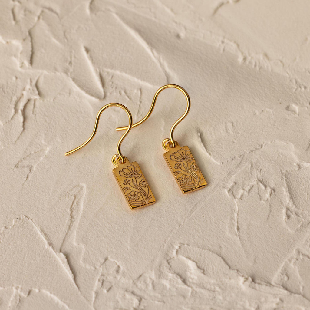 Rectangle Birth Flower Earrings featuring delicate floral engravings, perfect for personalizing your flower jewelry collection. Shown on a textured beige surface.