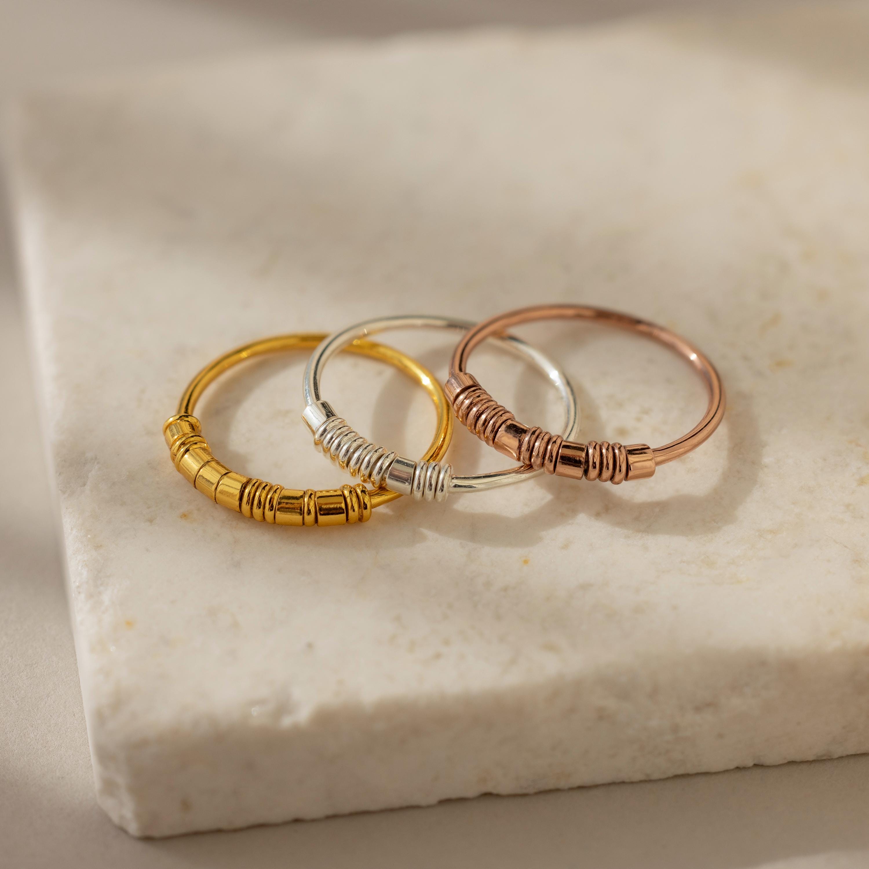 Three Dainty Morse Code Rings in gold, silver, and rose gold—ideal as personalized jewelry or a custom initial ring—are displayed on a white marble surface.