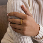 A hand with neatly manicured nails wears the Dainty Morse Code Ring, a personalized jewelry piece in gold, resting on the opposite arm in a ribbed cream sweater.