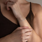 Someone in a brown tank top wears the Mama Tennis Letter Bracelet, delicately touching their wrist—ideal for fans of personalized jewelry and meaningful gift-giving.