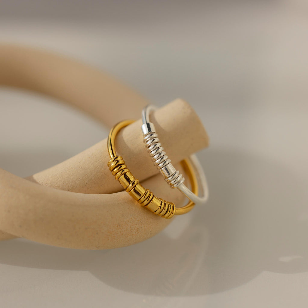 The Dainty Morse Code Ring features minimalist gold and silver bands with wrapped wire detail on a beige ceramic loop, ideal as personalized jewelry or a custom initial ring.