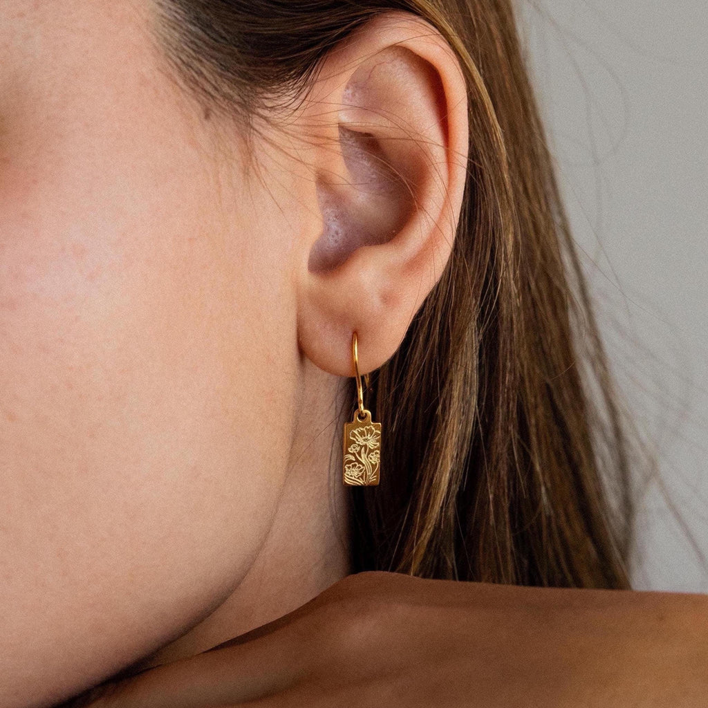 Close-up of a woman's ear wearing Rectangle Birth Flower Earrings—gold rectangular earrings with a floral design, ideal for fans of flower jewelry and personalized accessories.