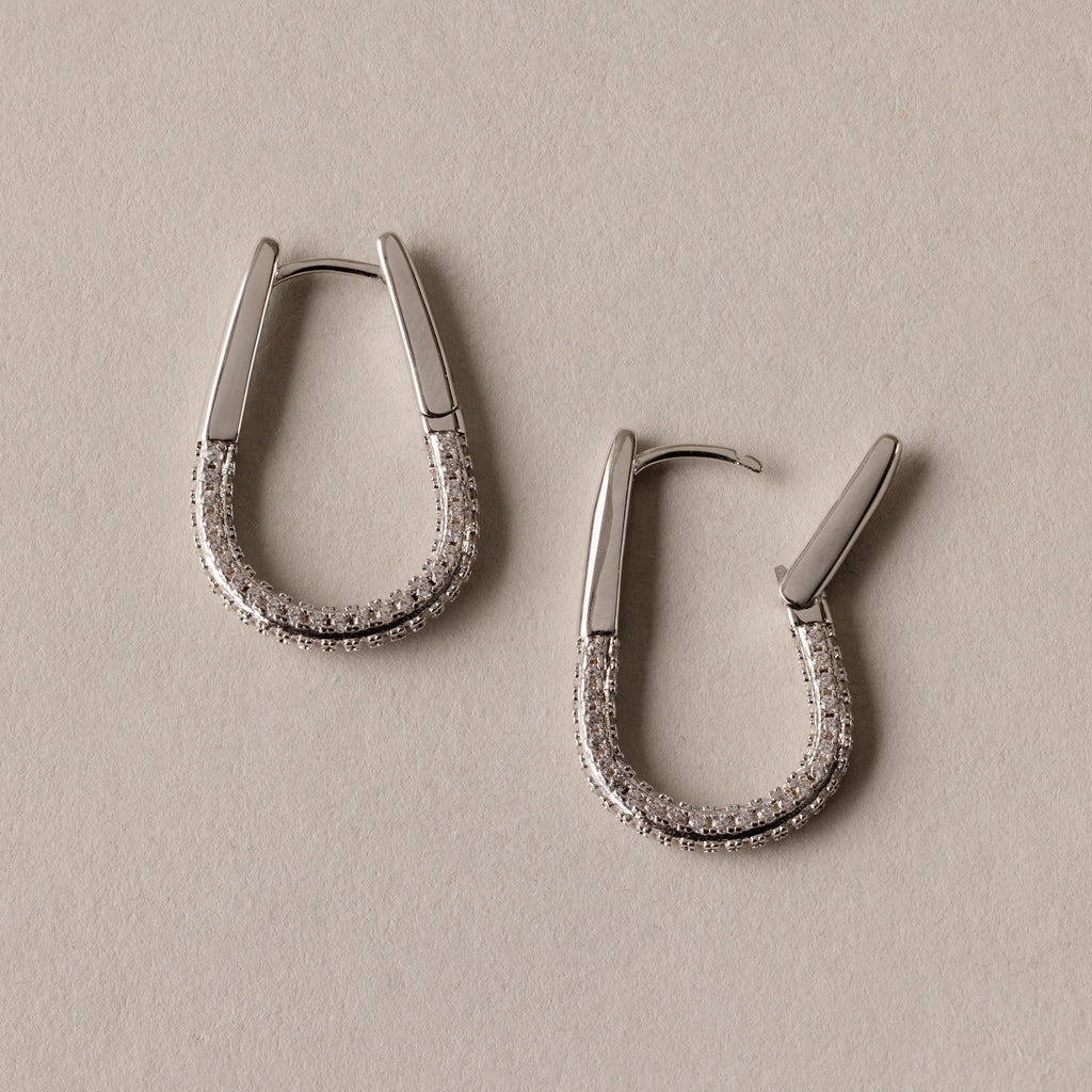 Bold Pave Oval Hoops, adorned with small sparkling stones, are displayed on a beige surface—perfect statement earrings for any occasion.