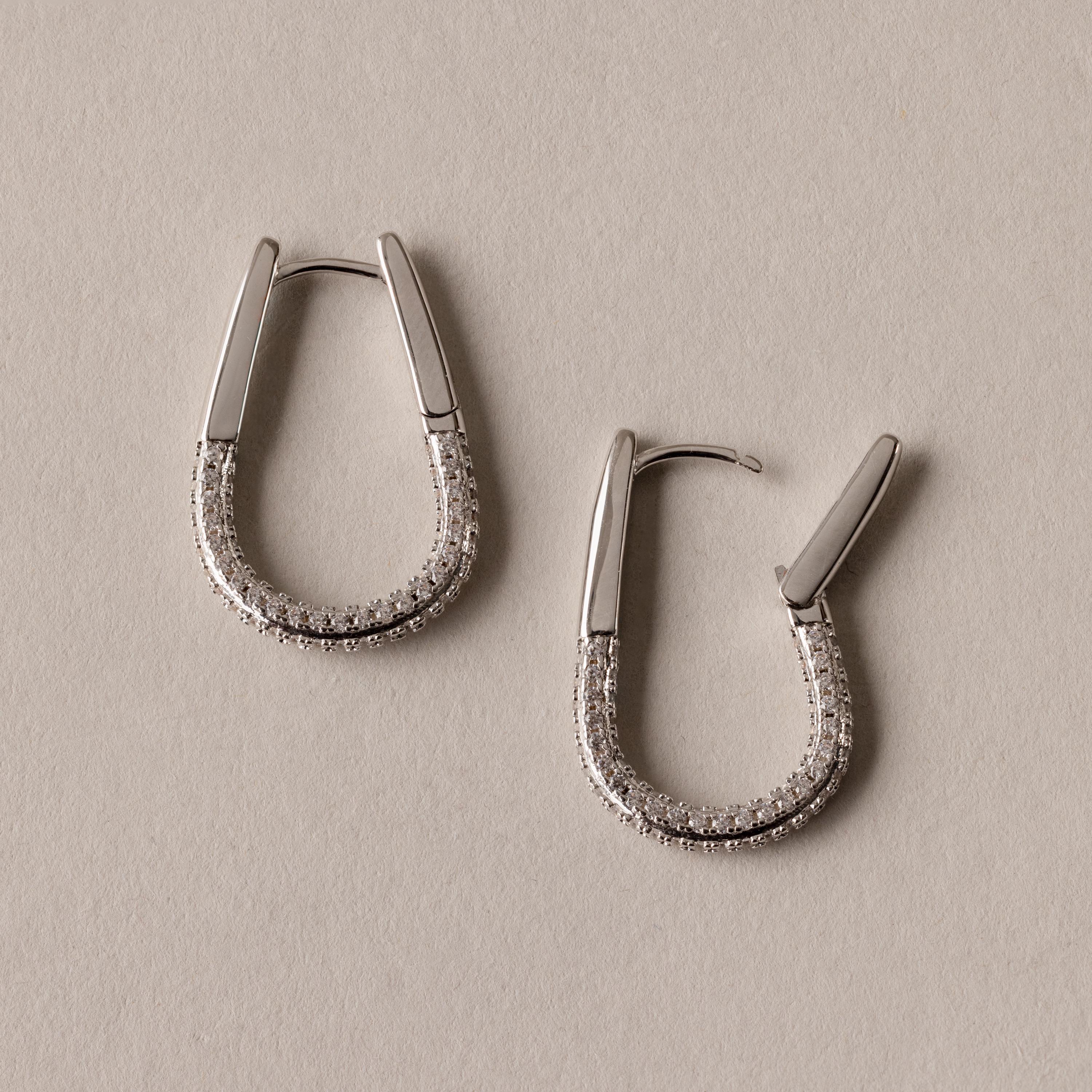 Bold Pave Oval Hoops, adorned with small sparkling stones, are displayed on a beige surface—perfect statement earrings for any occasion.