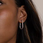 Close-up of a person’s ear wearing Bold Pave Oval Hoops—U-shaped silver hoops sparkling with small pave diamond gemstones.