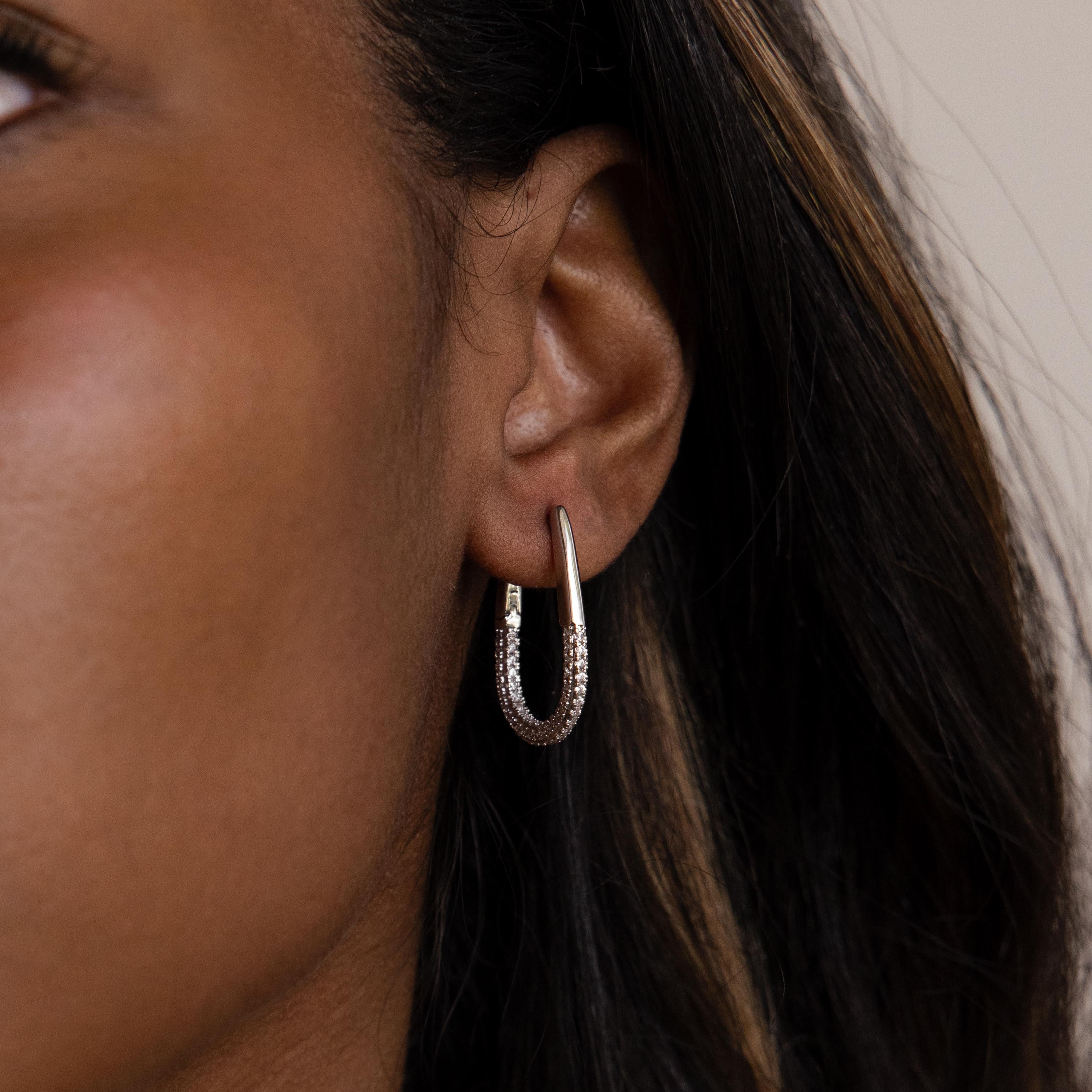 Close-up of a person’s ear wearing Bold Pave Oval Hoops—U-shaped silver hoops sparkling with small pave diamond gemstones.