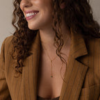Smiling woman in a brown pinstripe blazer wears the Initial Birthstone Lariat Necklace, a delicate gold lariat with a small pendant.