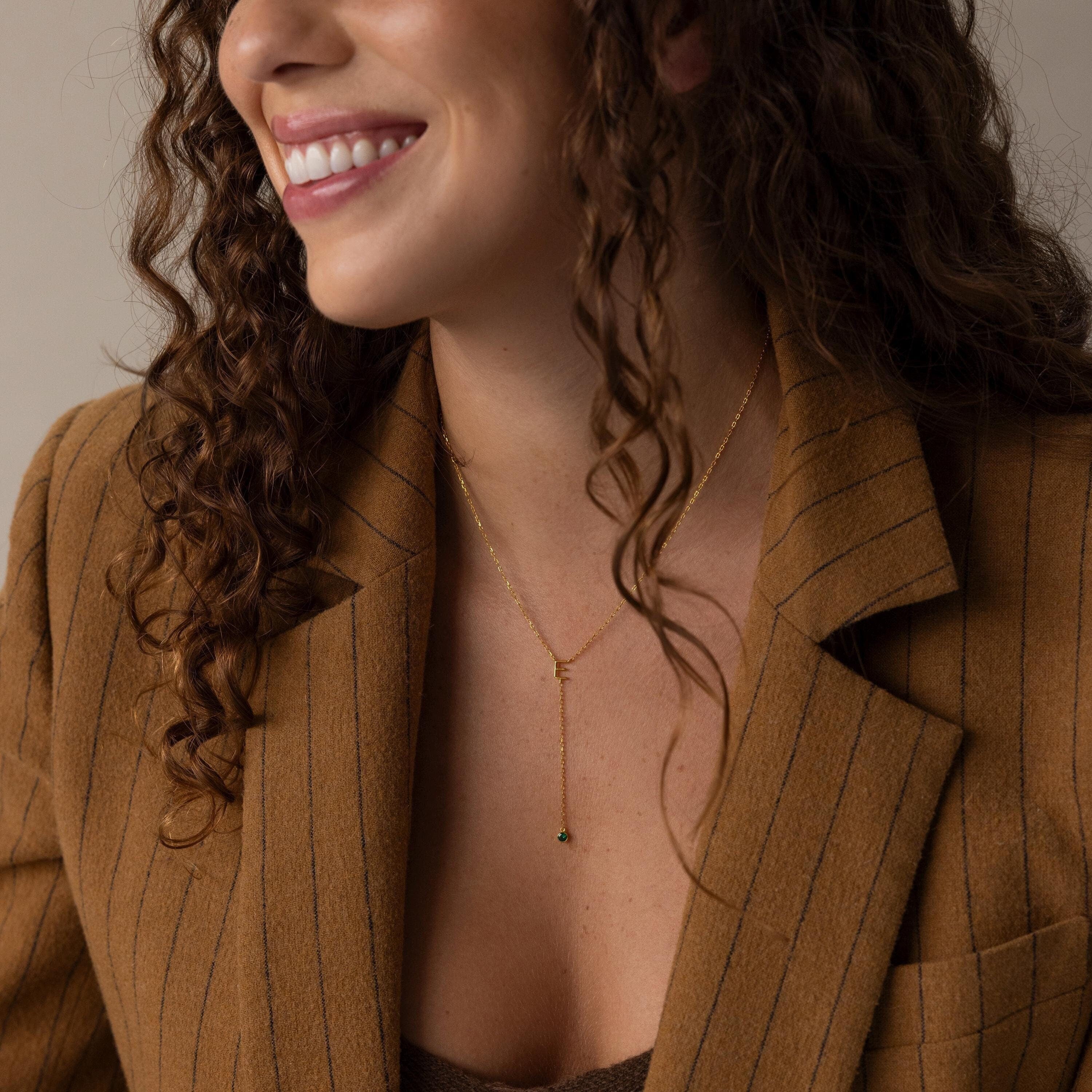 Smiling woman in a brown pinstripe blazer wears the Initial Birthstone Lariat Necklace, a delicate gold lariat with a small pendant.