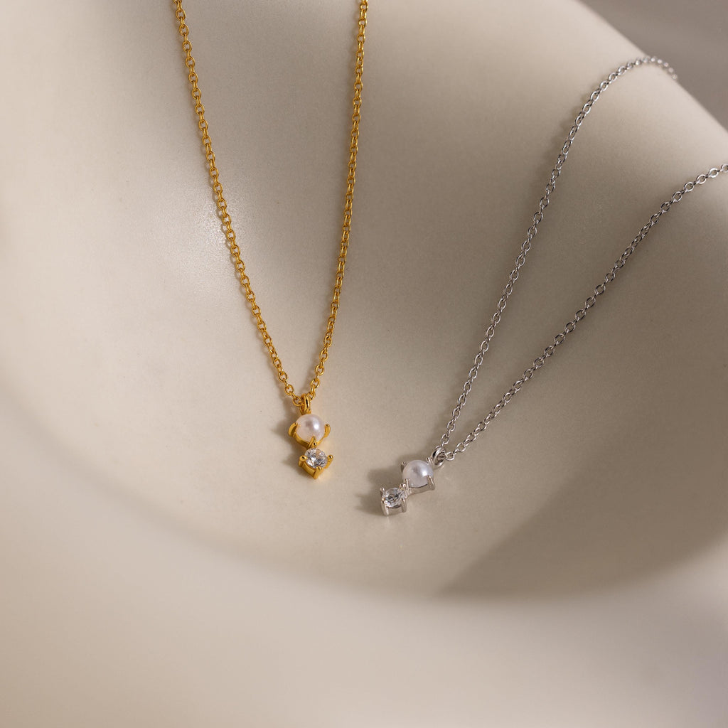 The Pearl Diamond Drop Necklace, along with other gold and silver bridal necklaces featuring pearl and crystal pendants, is displayed on a smooth beige surface.