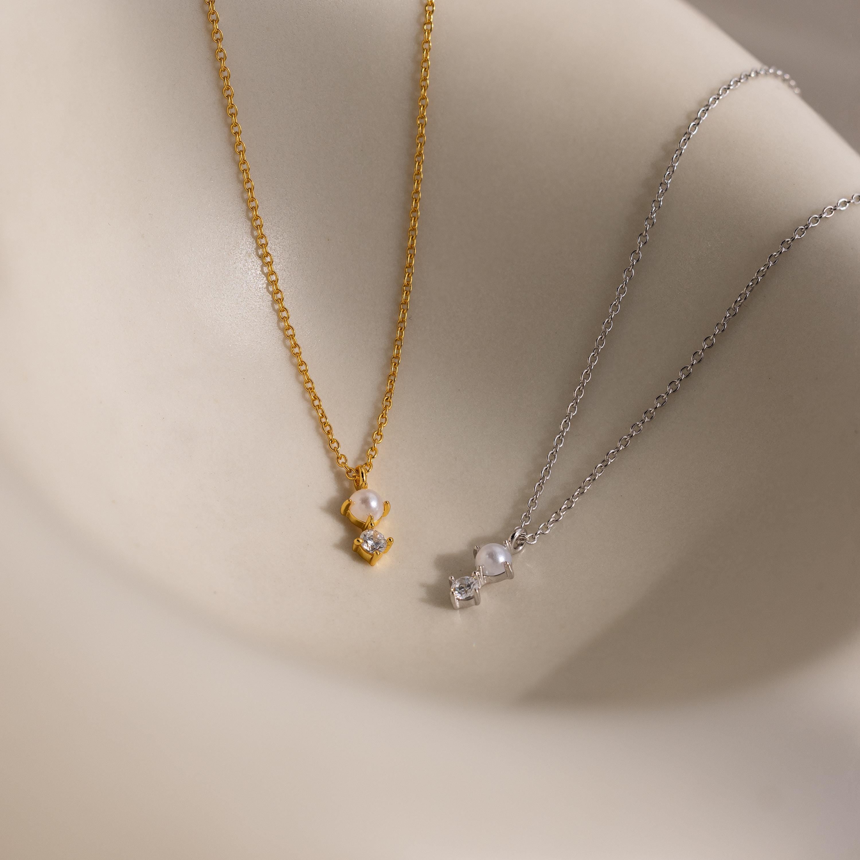 The Pearl Diamond Drop Necklace, along with other gold and silver bridal necklaces featuring pearl and crystal pendants, is displayed on a smooth beige surface.