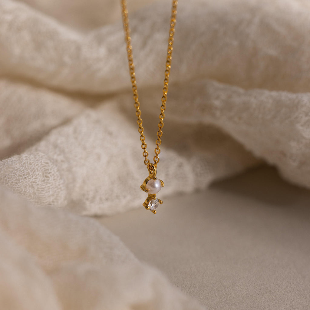 The Pearl Diamond Drop Necklace features a delicate pearl and crystal pendant, beautifully displayed on soft, light fabric—making it a perfect choice for an elegant bridal necklace.