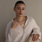 Woman in a cream ribbed sweater poses against a neutral background, wearing dainty jewelry including the Dainty Duo Pearl Necklace and stylish rings.