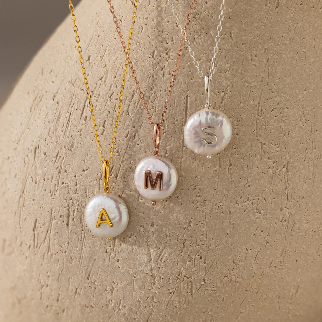 The Pearl Initial Pendant Necklace features a freshwater pearl on your choice of gold, rose, or silver chain, each with a personalized initial pendant—A, M, or S—for a unique accessory.