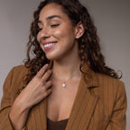 A smiling woman with curly hair, wearing a pinstripe blazer and the Pearl Initial Pendant Necklace, looks to the side.