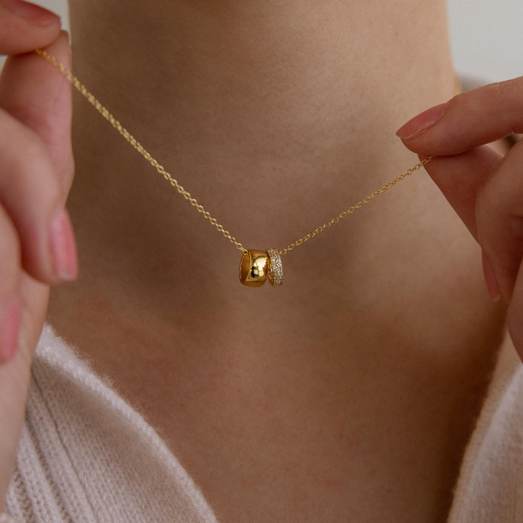Close-up of a person holding a dainty Pave Duo Circle Necklace with two pendants near their neck, paired with a light sweater.