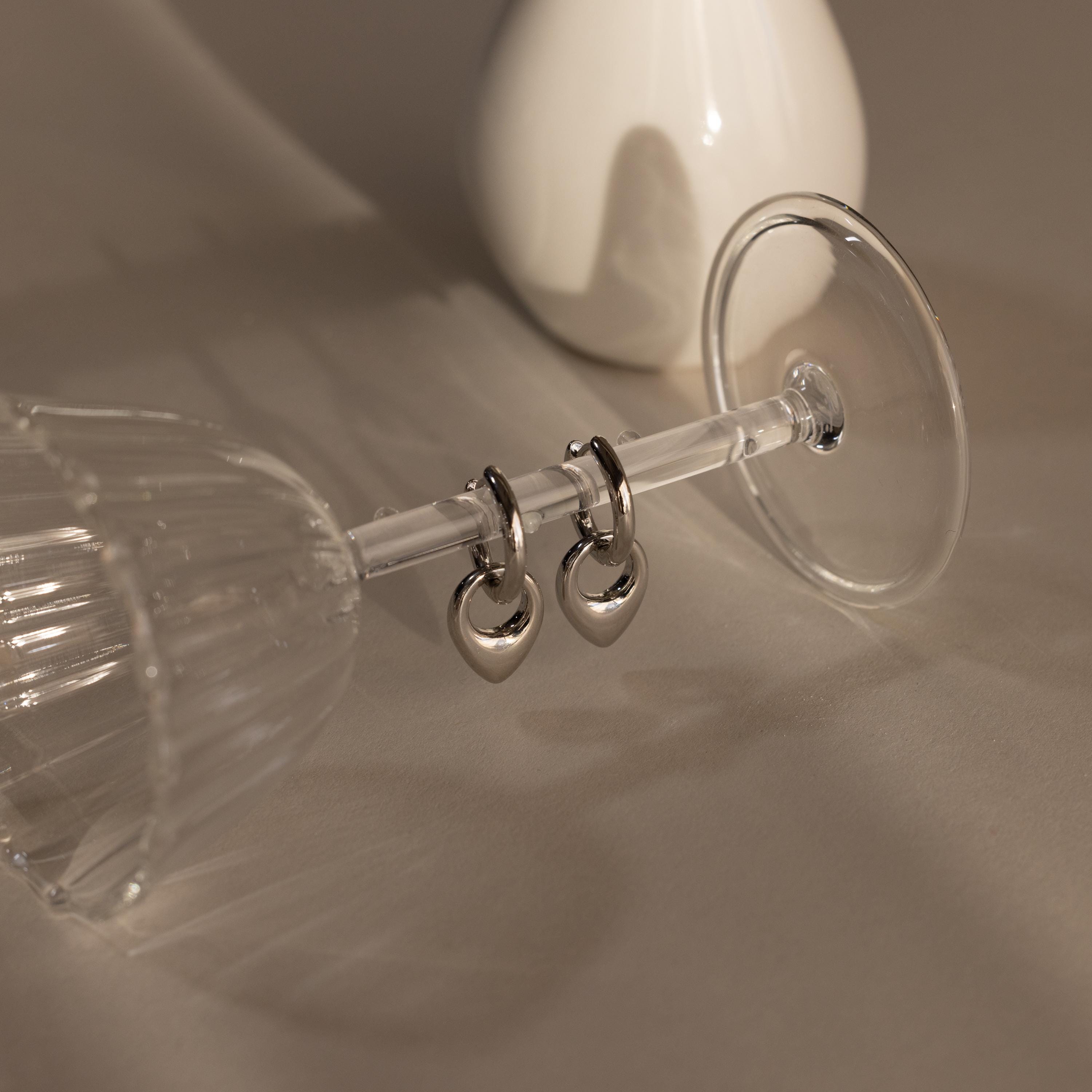 Bold Teardrop Hoops hang from the stem of an upside-down wine glass, with a white vase in the background—chic, versatile earrings ideal for any occasion.