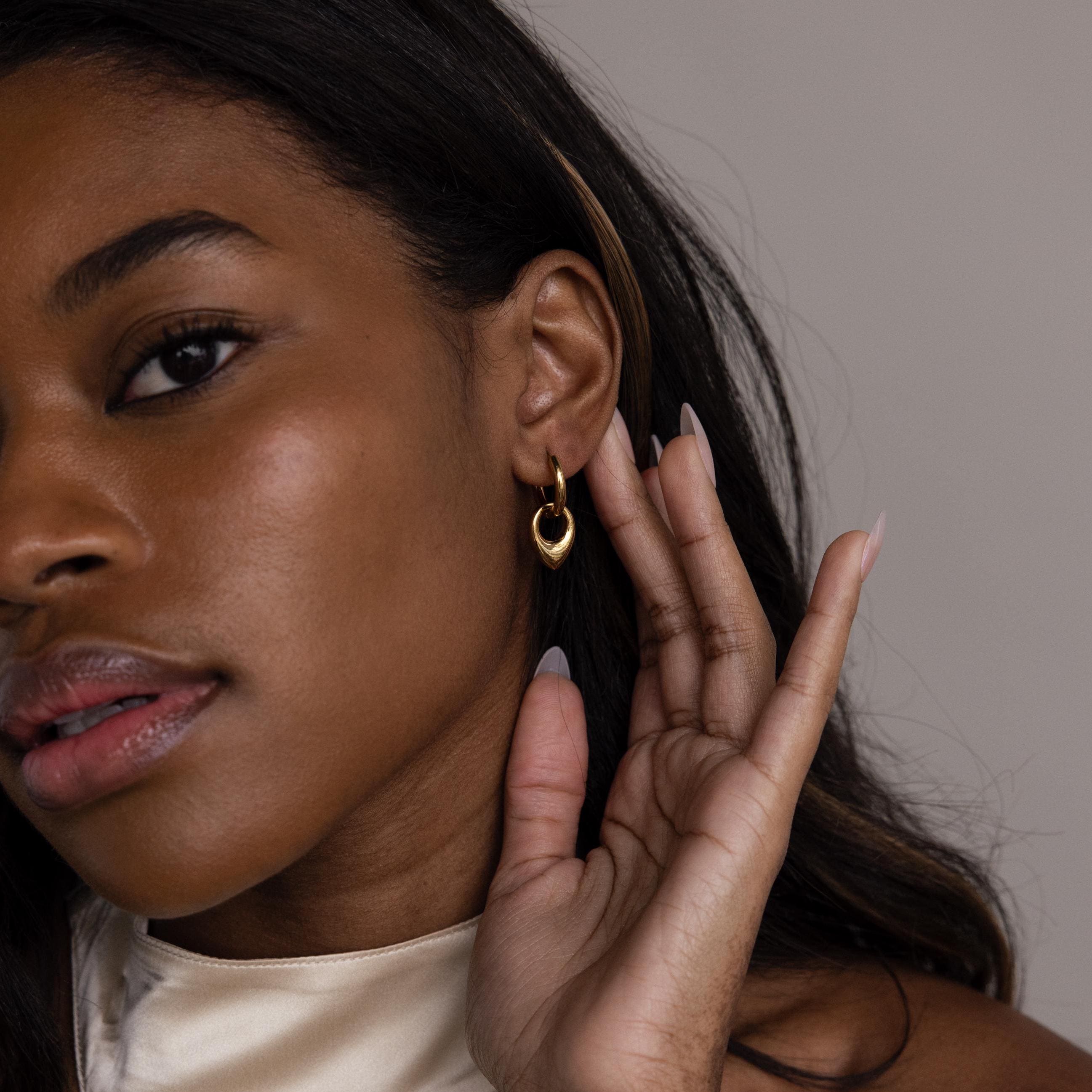 A woman with long hair gently touches her Bold Teardrop Hoops, highlighting the earrings’ versatile and striking design.