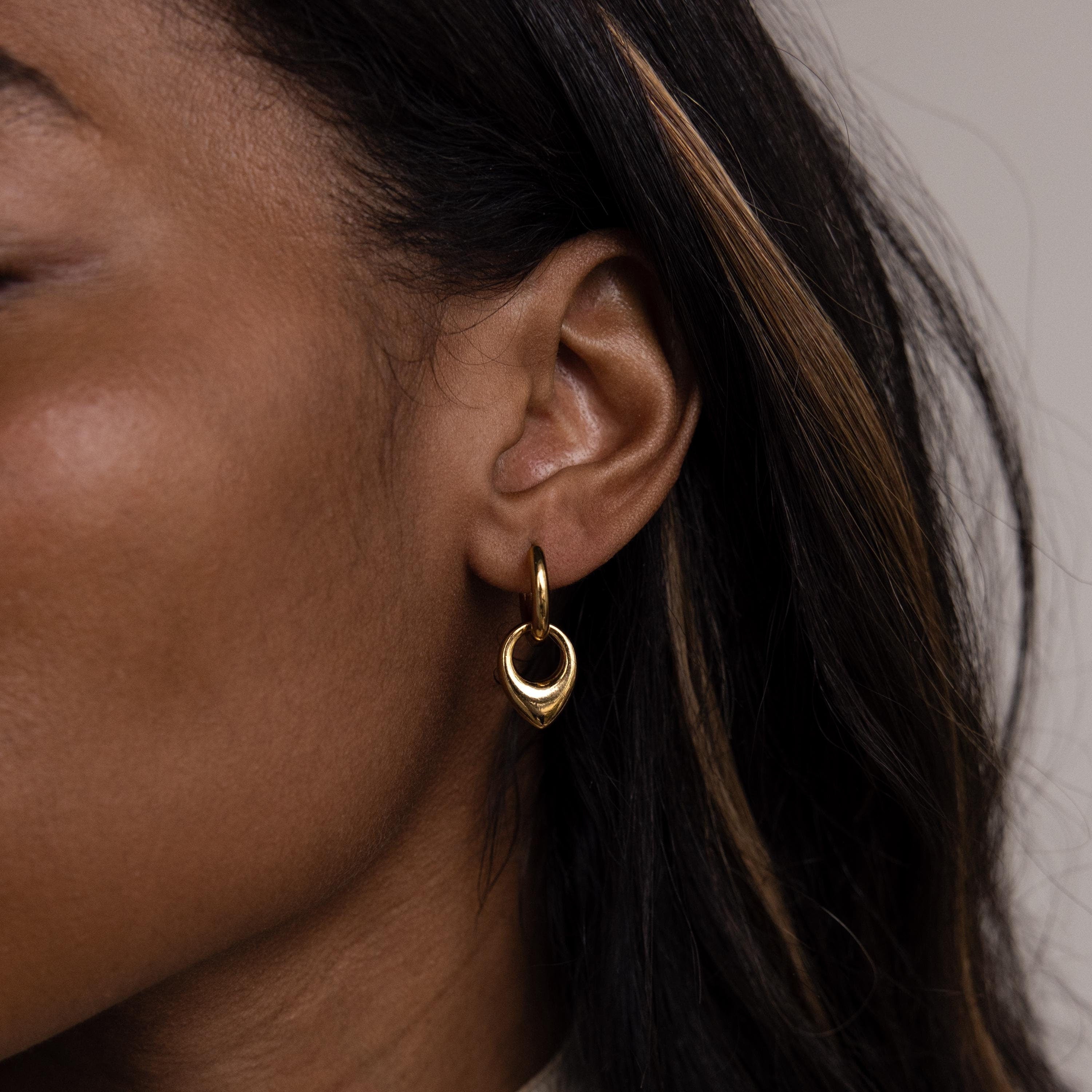 Close-up of a woman's ear with brown, highlighted hair wearing Bold Teardrop Hoops—versatile gold earrings perfect for any occasion.
