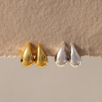 Chunky Tear Drop Studs in gold and silver shown side by side on textured beige paper, highlighting their elegant, oversized teardrop design.