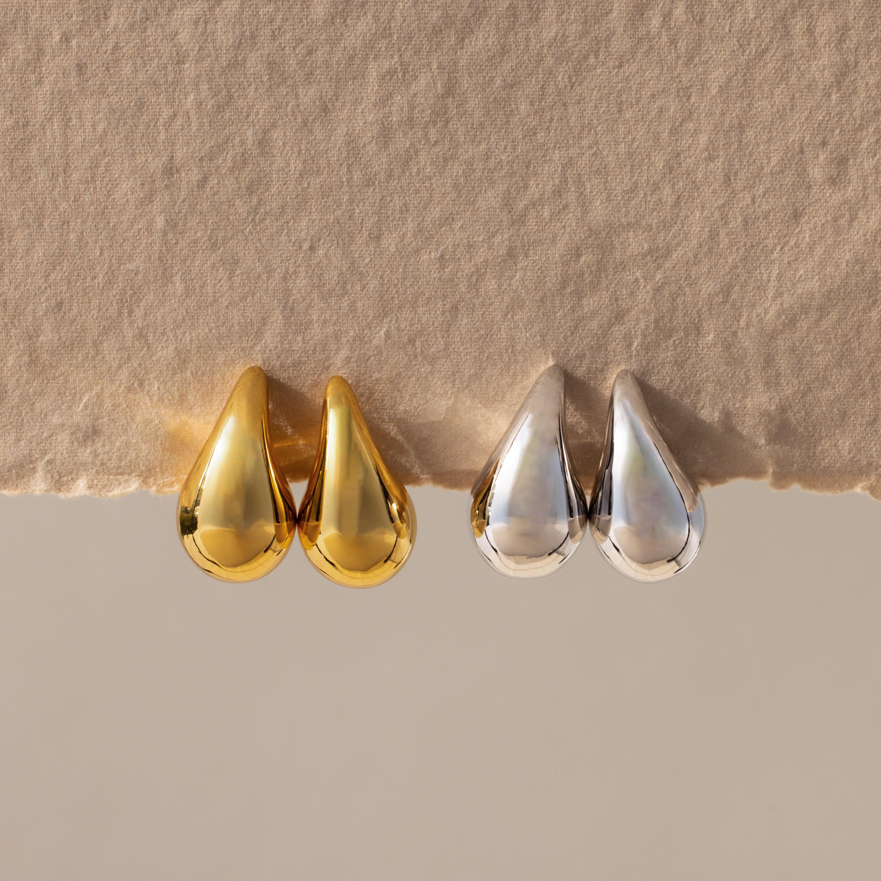Chunky Tear Drop Studs in gold and silver shown side by side on textured beige paper, highlighting their elegant, oversized teardrop design.