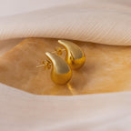 Chunky Tear Drop Studs: Gold teardrop-shaped earrings showcased on a golden surface with soft white fabric, these studs bring effortless elegance to any outfit.