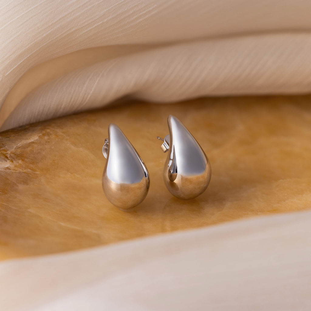 Chunky Tear Drop Studs are featured on a beige marble surface, with a background of soft fabric.