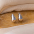 Chunky Tear Drop Studs are featured on a beige marble surface, with a background of soft fabric.