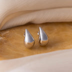 Chunky Tear Drop Studs are featured on a beige marble surface, with a background of soft fabric.
