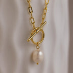 The Paperclip Pearl Toggle Necklace features a gold chain with a single pearl pendant, offering a modern take on elegant pearl jewelry, showcased against a soft white background.