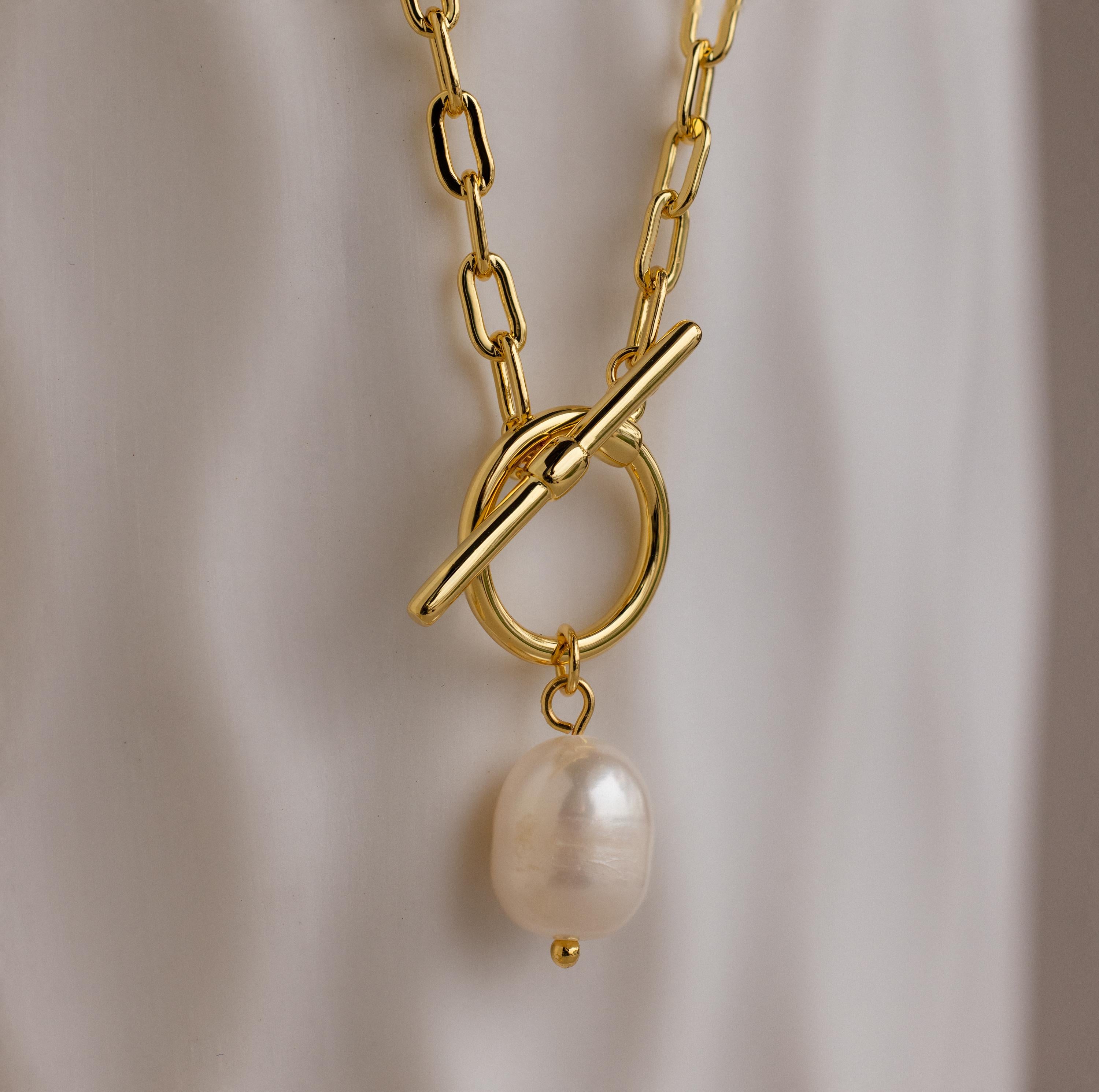 The Paperclip Pearl Toggle Necklace features a gold chain with a single pearl pendant, offering a modern take on elegant pearl jewelry, showcased against a soft white background.