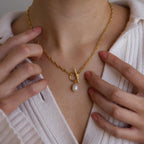 Close-up of a person wearing the Paperclip Pearl Toggle Necklace, featuring a toggle clasp and pearl pendant, styled with a white ribbed top.