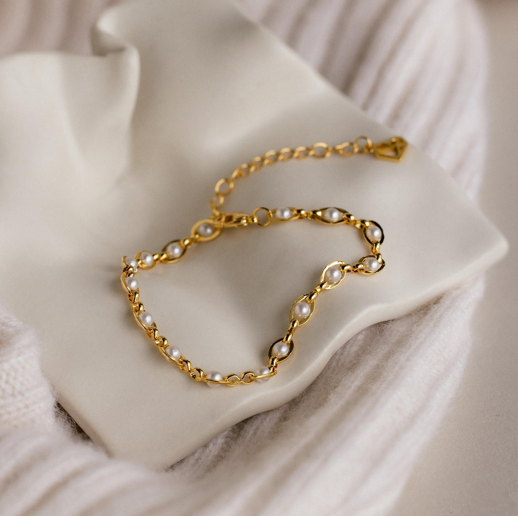The Eternity Pearl Bracelet is elegantly displayed on a white ceramic dish with a soft textured fabric background.