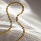 An Engraved Herringbone Name Necklace with CHARLOTTE rests on a softly lit, light-colored surface, radiating elegance and personal charm.