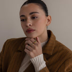 A woman in a brown pinstripe blazer touches her face, thoughtfully showcasing the Toi et Moi Princess Birthstone Ring against a plain background.