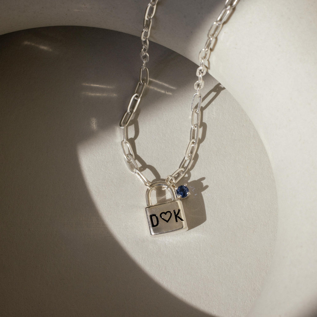 Initial Birthstone Padlock Necklace with a personalized pendant engraved D ♥ K and a small blue gemstone that shimmers in sunlight.