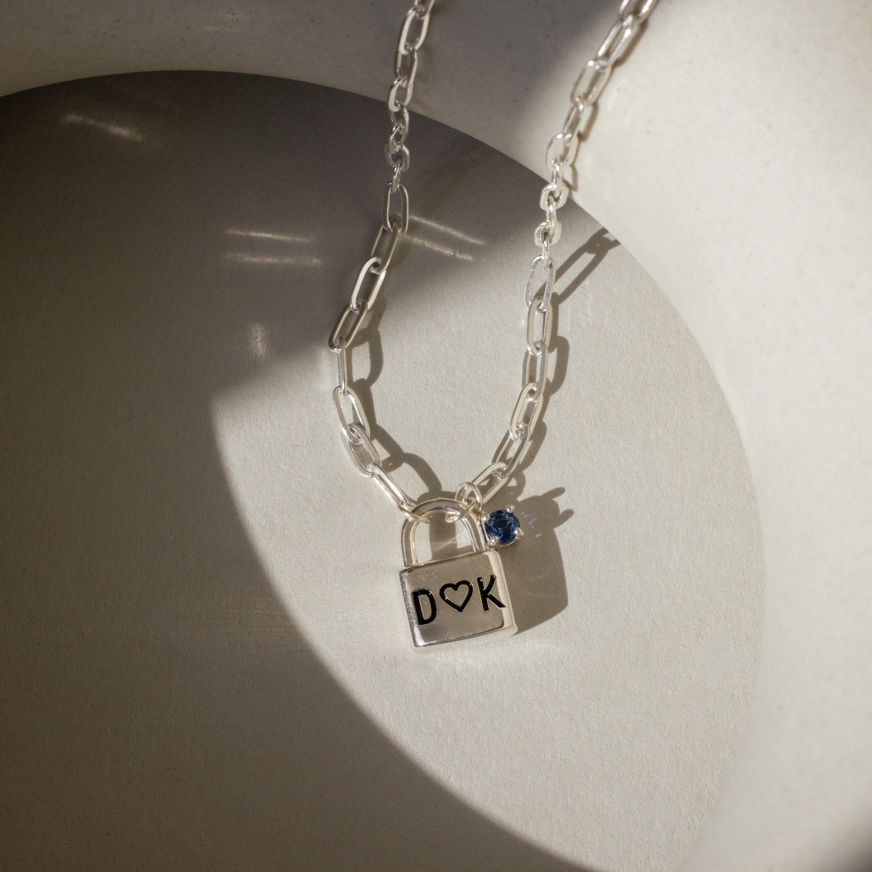 Initial Birthstone Padlock Necklace with a personalized pendant engraved D ♥ K and a small blue gemstone that shimmers in sunlight.