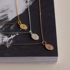 The Pave Initial Pendant Necklace, with its teardrop shape and sparkling design, shines elegantly in gold, silver, and rose gold on a black and white book.