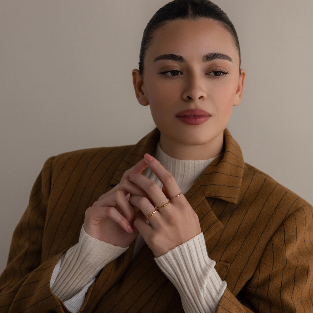 Woman in a brown pinstripe blazer and white top, wearing the Toi et Moi Baguette Birthstone Ring and gold rings, looking to the side.