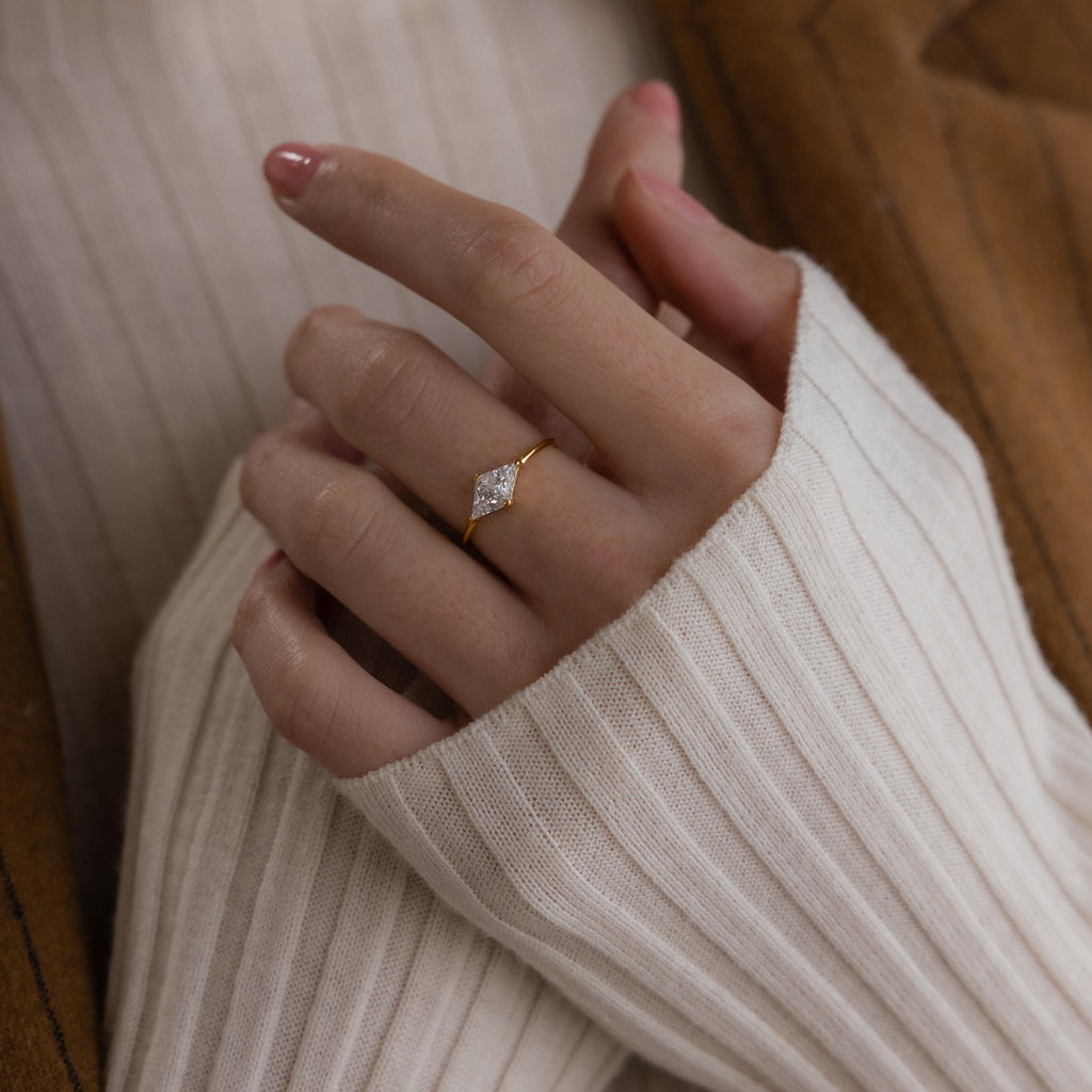 A hand wearing the Toi et Moi Triangle Birthstone Ring, paired with a cream ribbed sweater and a brown jacket.