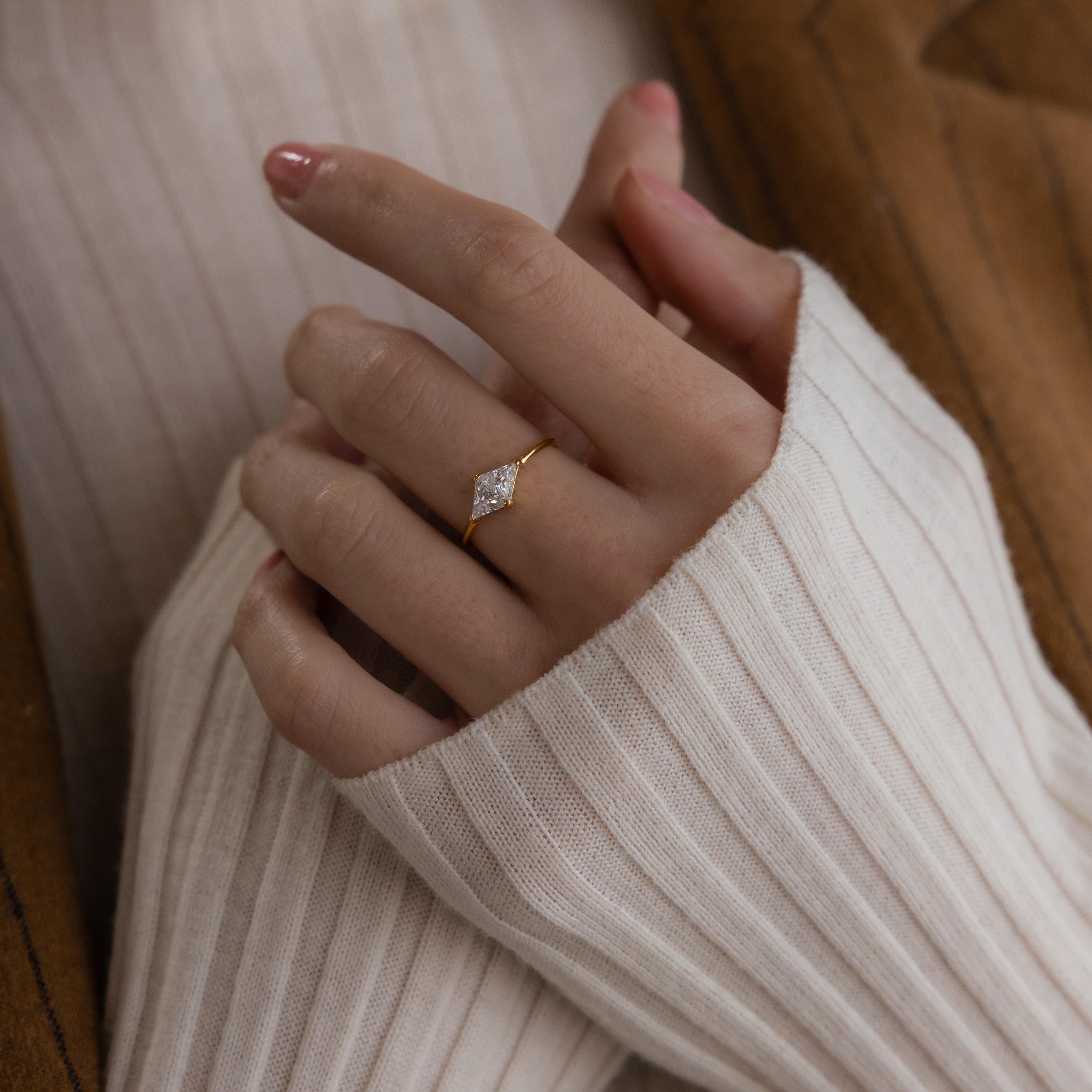 A hand wearing the Toi et Moi Triangle Birthstone Ring, paired with a cream ribbed sweater and a brown jacket.