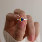 A hand holds the Toi et Moi Triangle Birthstone Ring, featuring yellow and blue triangular gemstones in a striking geometric silver setting.