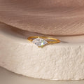 Toi et Moi Triangle Birthstone Ring displayed on a textured white surface, with soft peach fabric in the background.