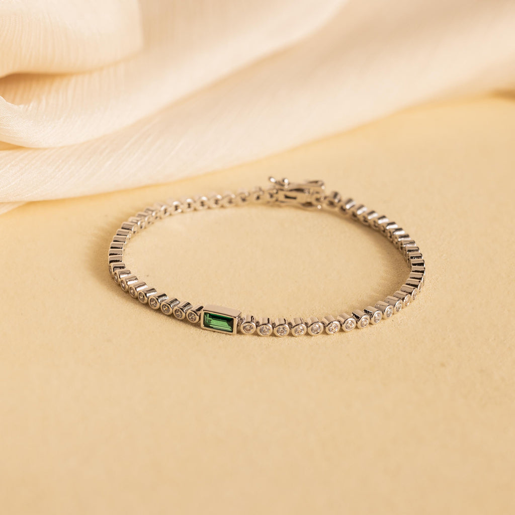Emerald Baguette Tennis Bracelet: Showcasing a vibrant green gemstone and sparkling CZ diamonds, this elegant statement piece is displayed on a beige fabric background.