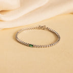 Emerald Baguette Tennis Bracelet: Showcasing a vibrant green gemstone and sparkling CZ diamonds, this elegant statement piece is displayed on a beige fabric background.