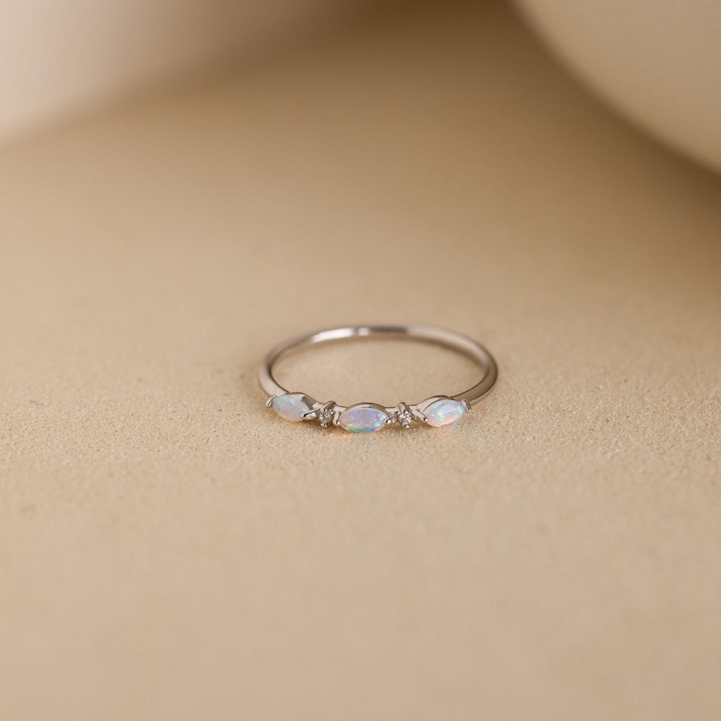 A close-up of the Alessia Trio Opal Ring in silver, featuring three marquise-cut opals accented with tiny diamonds on a slim silver band, displayed against a neutral beige background.